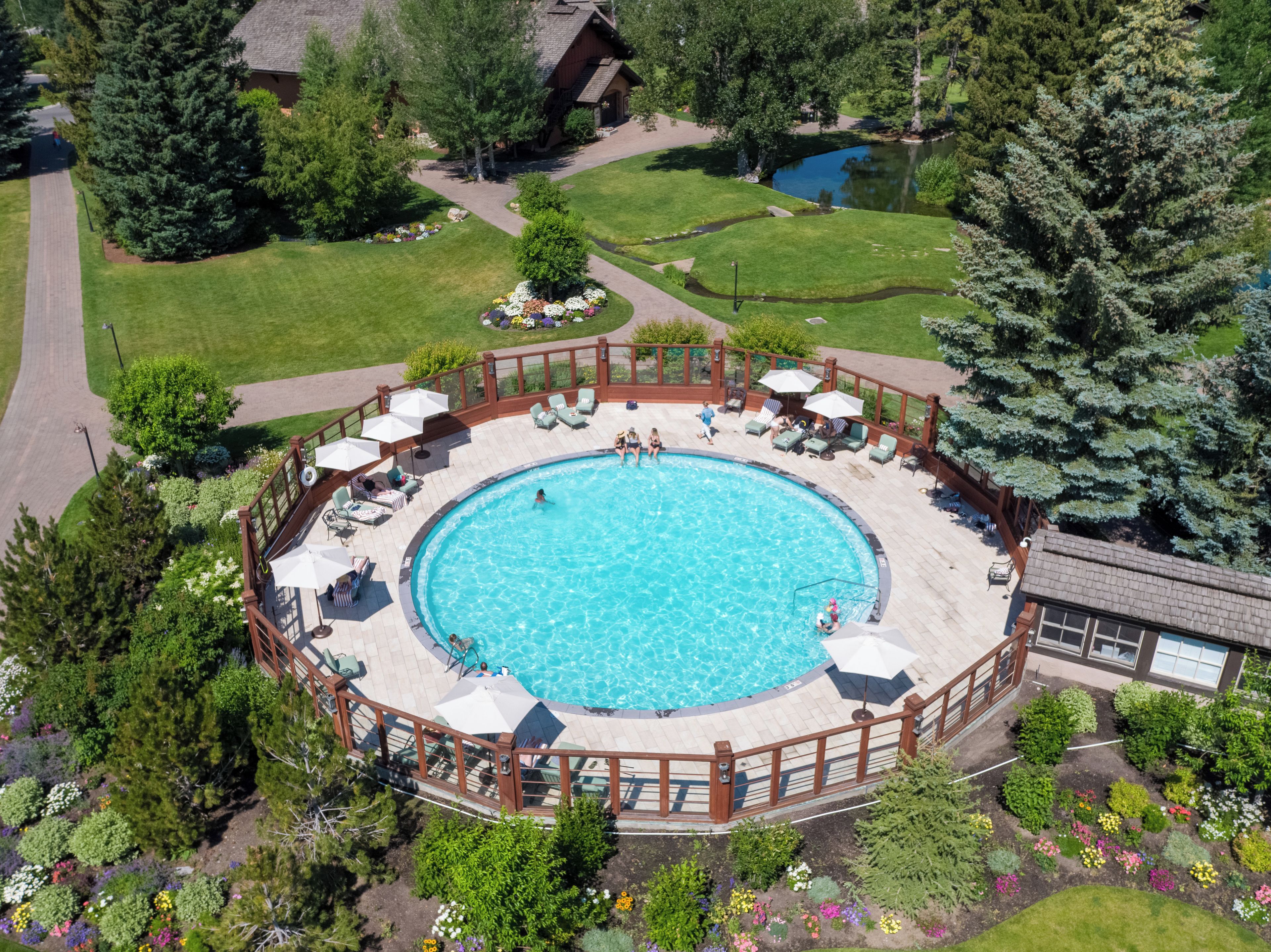 A circular pool with a wooden deck and lounge chairs, surrounded by a garden with various plants and flowers.