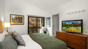 Una camera da letto con un letto, una televisione, una cassettiera e una finestra vista alberi.