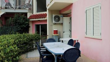 A patio with a table and chairs, a red-tiled roof, and a pink wall with shutters.