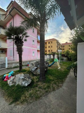 Ein Wohngebäude mit rosafarbenem Mauerwerk, einer Palme und einem Spielplatz mit Rutsche.