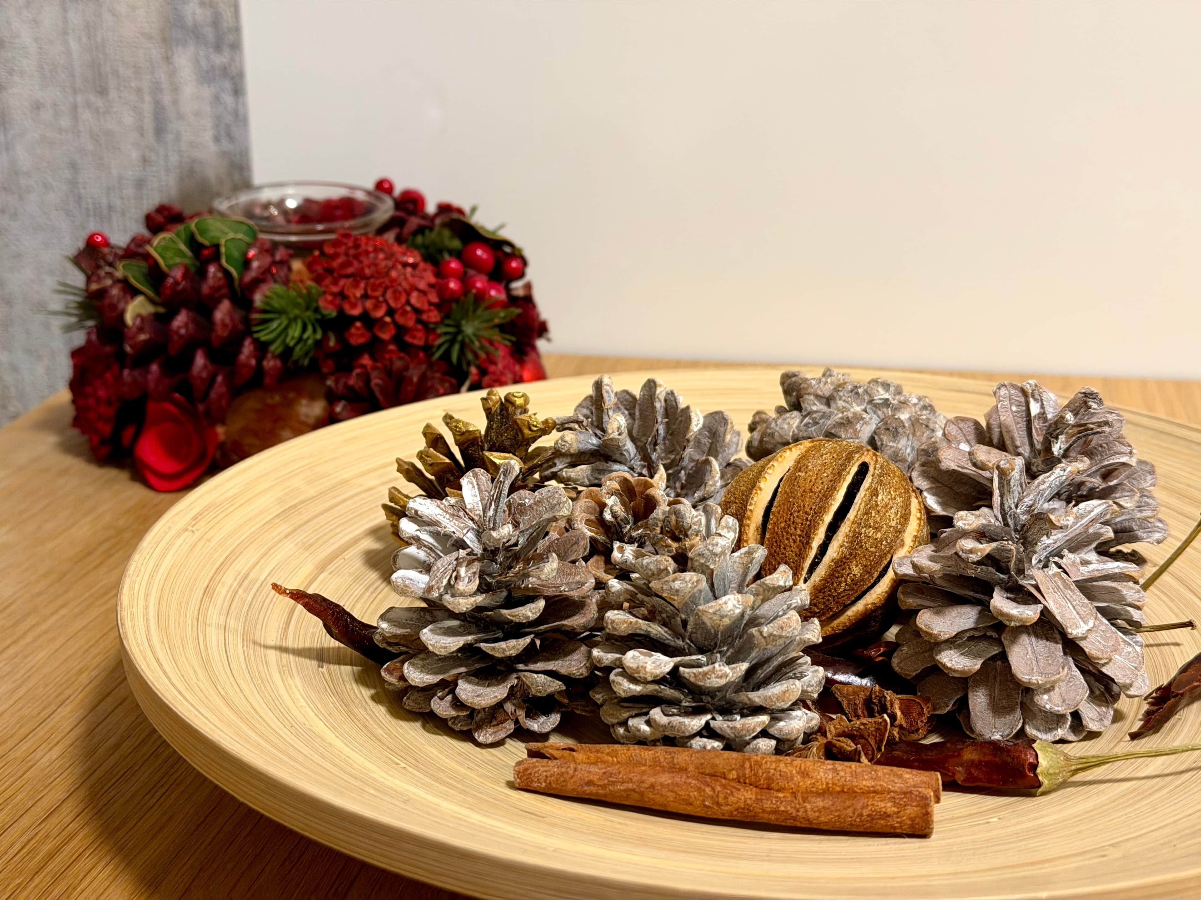 A wooden table with pine cones, cinnamon sticks, and dried red berries.