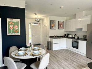 A modern kitchen with white cabinets, a built-in oven, and a dining area with a round table set for four. - HomiHost-Apricot House (Birmingham)