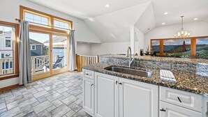 A spacious kitchen with a granite countertop, white cabinets, and a large window with curtains. - Big Blue (North) | 1,625 ft to the beach | Dog Friendly and Community Pool (Corolla)