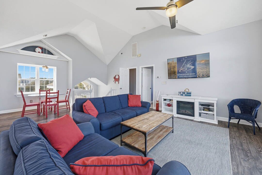 A spacious living room with a blue sofa, red cushions, a wooden coffee table, and a white entertainment unit.