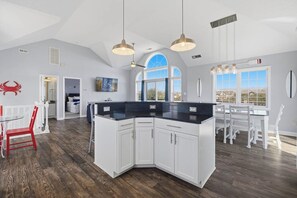 A spacious kitchen with a large island, white cabinetry, and a dining area with a white table and chairs. - Fiddlin Around | Private Pool and Hot Tub | Mackerel Beach Access (Corolla)