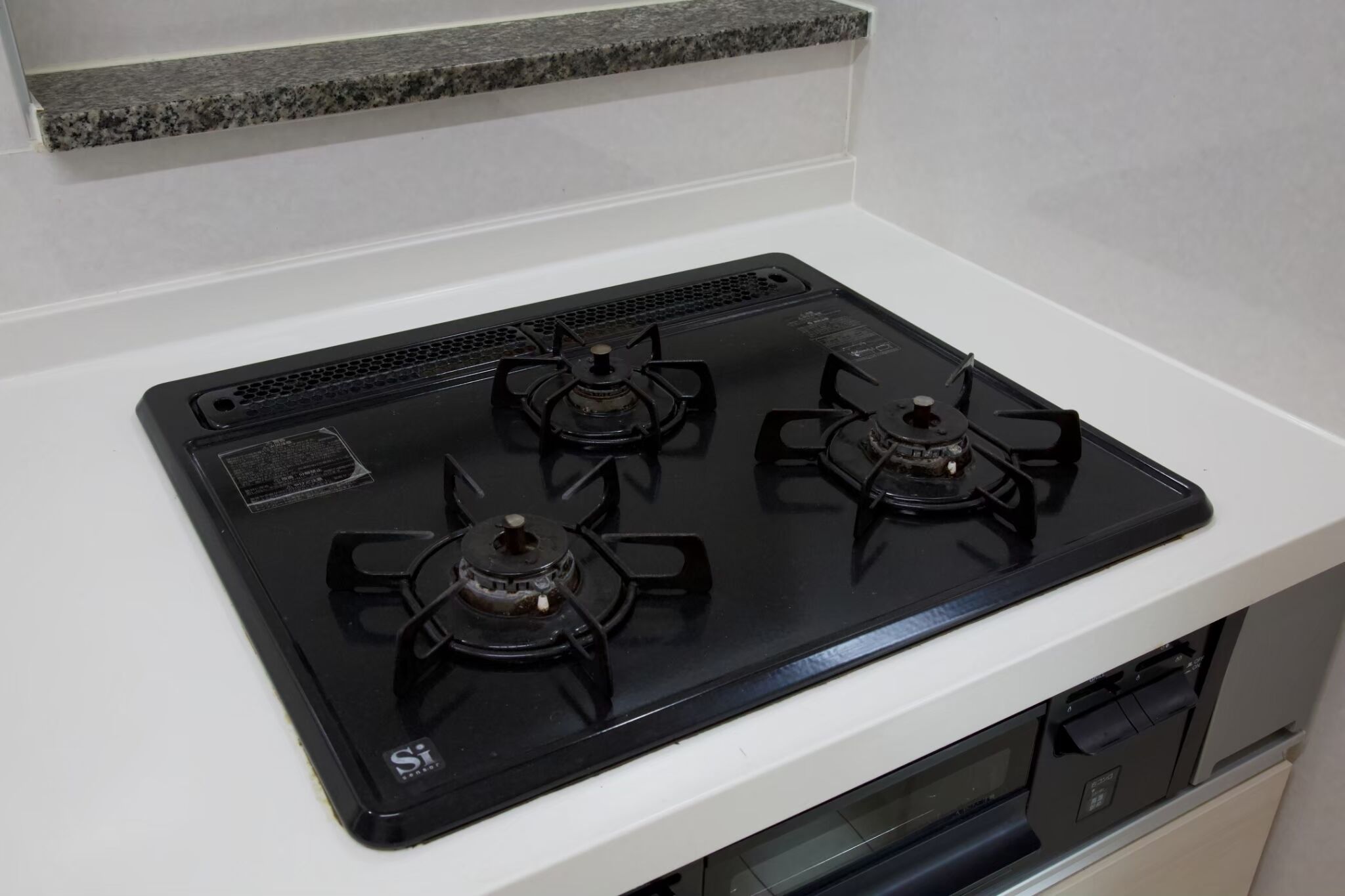 Une cuisine avec une plaque de cuisson noire, un plan de travail blanc et un pare-feu en granit.
