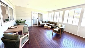 A sunlit room with a wooden deck, a dining table with chairs, a sofa, and a large window with a view. - Catalina's at Corlette, steps to the beach (Corlette)