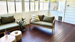 A covered porch with wooden flooring, two green cushioned sofas, a small round table with two wine glasses and a bottle, and a potted plant. - Catalina's at Corlette, steps to the beach (Corlette)
