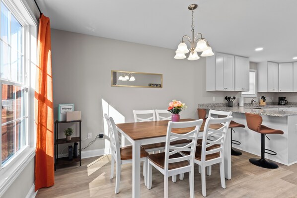 A modern kitchen with white cabinets, a wooden dining table with white chairs, and a pendant light. - Stylish 6 bd/4.2bth Duplex, Charming Location Near the Action! (Kannapolis)
