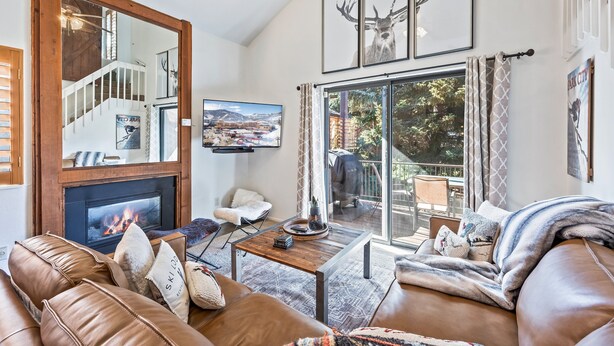 A living room with a fireplace, leather sofa, and a large window with curtains. - Walk to Canyons Village Charm: Vintage-Inspired Interiors, Private Patio,  Shared Pool (Park City)