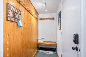 A wooden wall with a sign that reads "NO SKI BOOT BEYOND THIS POINT." A bench with folded towels is placed against the wall, and a door with a security lock is visible. - Walk to Canyons Village Charm: Vintage-Inspired Interiors, Private Patio,  Shared Pool (Park City)