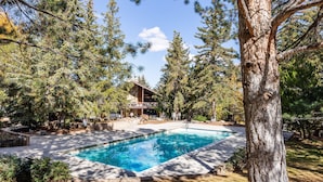 A rectangular swimming pool surrounded by trees, with a building in the background. - Walk to Canyons Village Charm: Vintage-Inspired Interiors, Private Patio,  Shared Pool (Park City)