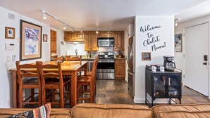 A modern kitchen with wooden cabinets, stainless steel appliances, and a dining area with a wooden table and chairs. - Walk to Canyons Village Charm: Vintage-Inspired Interiors, Private Patio,  Shared Pool (Park City)