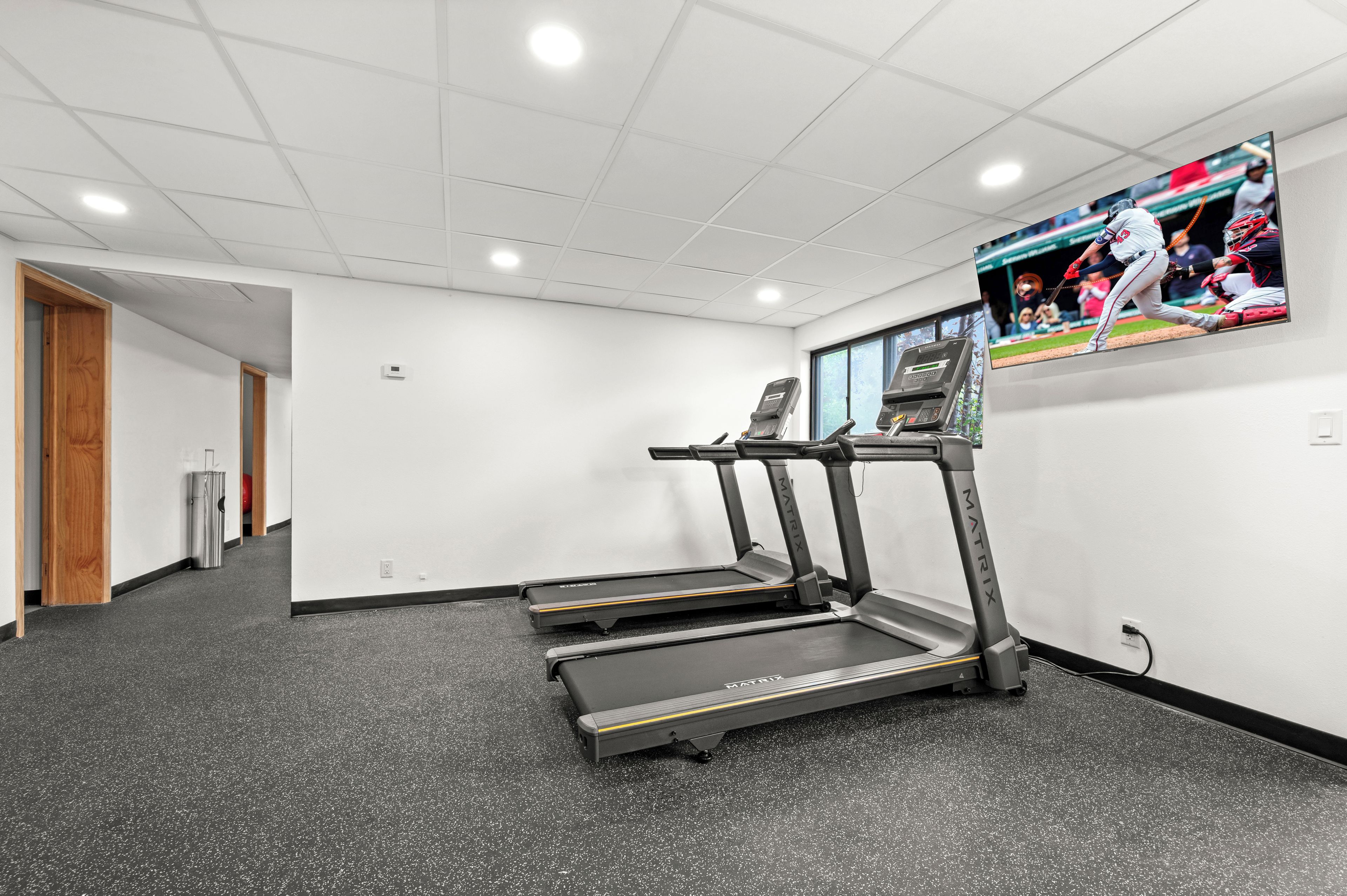 A fitness room with treadmills, a television, and a door leading to another area.