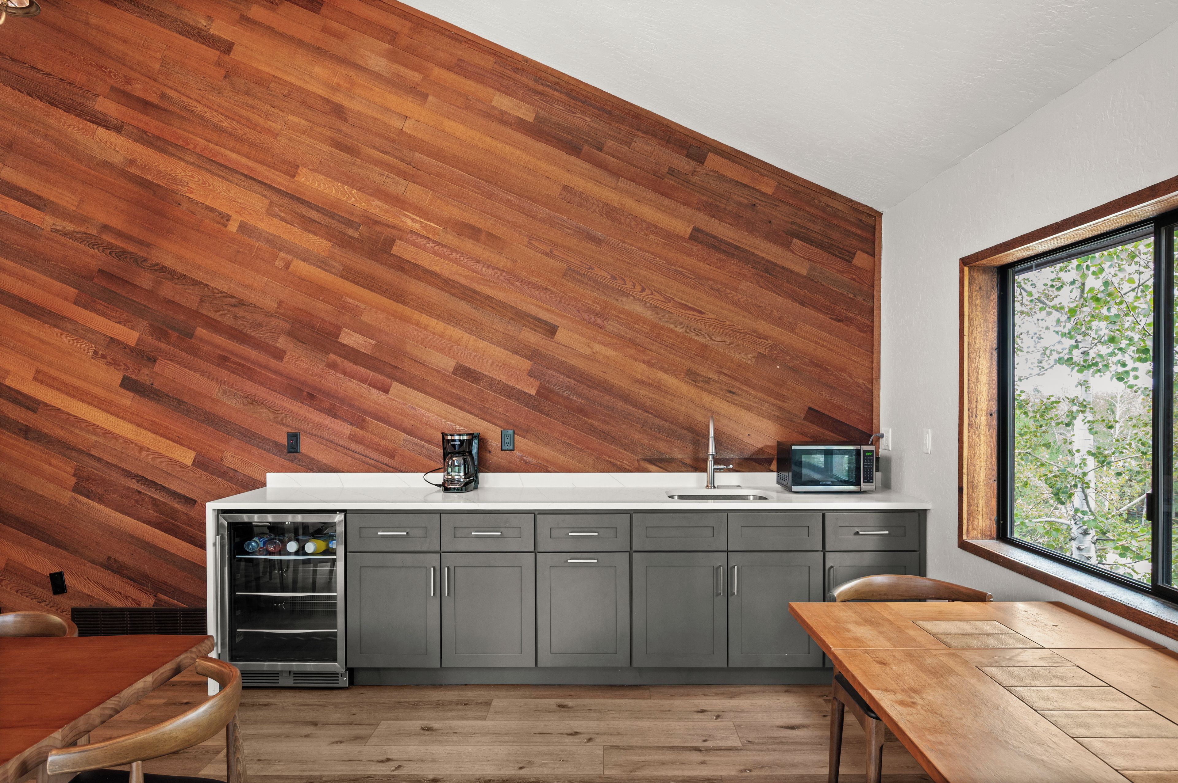 A modern kitchen with a wooden wall, grey cabinets, a white countertop, and a window with a view.