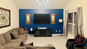 Un salon avec un mur d’accent bleu, un téléviseur à écran plat, un canapé, une table basse et un lampadaire.