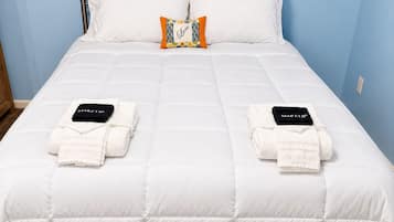 Una cama bien tendida con ropa blanca, dos toallas y una almohada con diseño floral.