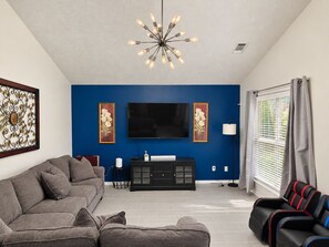 A living room with a blue accent wall, a flat-screen TV, a modern chandelier, a sofa, a coffee table, and a massage chair.