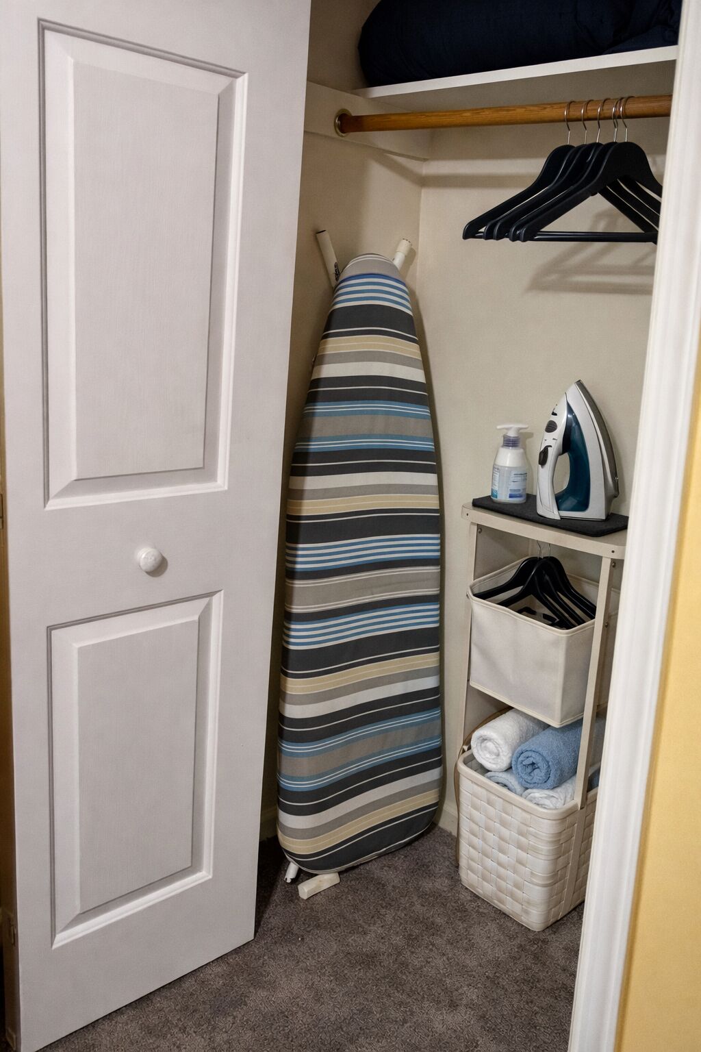 A closet with a hanging rack, an ironing board, and storage baskets.