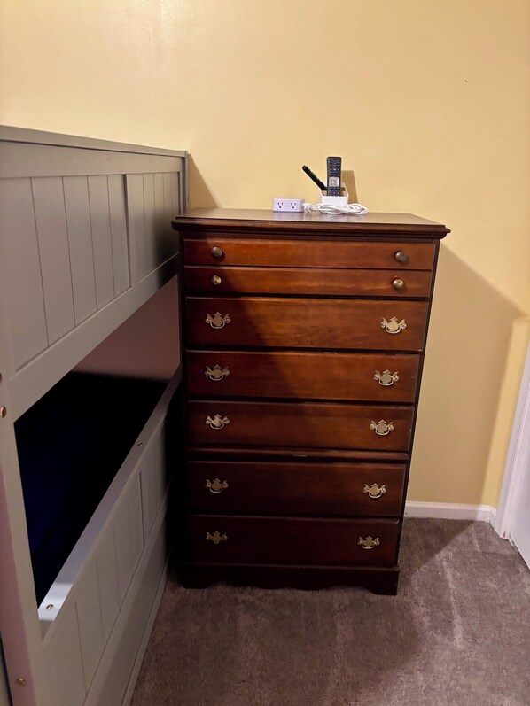 A wooden dresser with drawers and a small shelf on top, against a plain wall.