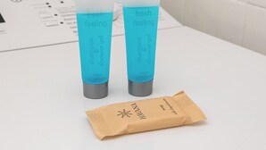 Dos botellas de champú y acondicionador con etiqueta 'fresh feeling' sobre una superficie blanca, con una bolsa de papel marrón al frente.