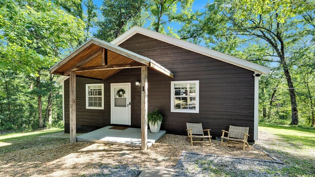 A rustic cabin with a covered porch, a front door, and two wicker chairs outside. - Fantastic 3-bedroom home near great trails in Bella Vista (Bella Vista)