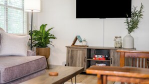 A living room with a sofa, a coffee table, a TV mounted on the wall, a floor lamp, and a bookshelf with books and decorative items. - Fantastic 3-bedroom home near great trails in Bella Vista (Bella Vista)