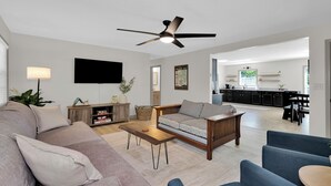 A modern living room with a sofa, coffee table, and a ceiling fan. A kitchen is visible in the background. - Fantastic 3-bedroom home near great trails in Bella Vista (Bella Vista)