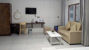 A modern living room with a sofa, a coffee table, a TV, a wooden chair, a desk, and a wardrobe. - Empire House Phnom Penh (Phnom Penh)