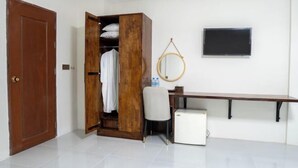 A room with a wooden wardrobe, a desk, a chair, a small white refrigerator, a round mirror, and a television on the wall. - Empire House Phnom Penh (Phnom Penh)