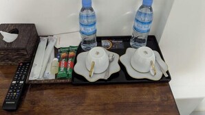 A tray with two water bottles, two white cups with gold trim, a remote control, a tissue box, and some snacks. - Empire House Phnom Penh (Phnom Penh)