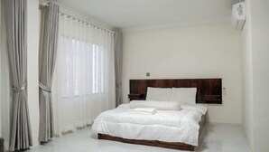 A bedroom with a wooden headboard, white bedding, and a large window with sheer curtains. - Empire House Phnom Penh (Phnom Penh)