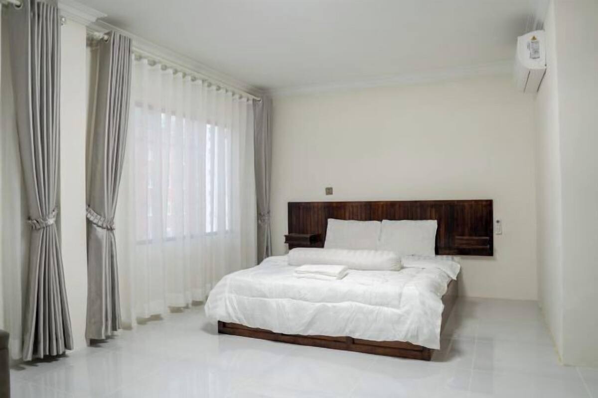 A bedroom with a wooden headboard, white bedding, and a large window with sheer curtains.