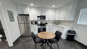 Une cuisine moderne avec des meubles blancs, des appareils en acier inoxydable et une table ronde en bois, accompagnée de chaises noires.