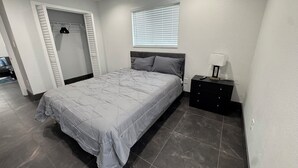 Une chambre à coucher comprenant un lit, une table de chevet, une fenêtre avec des stores et une armoire avec une porte coulissante.