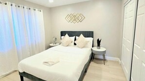 Ένα υπνοδωμάτιο με ένα κρεβάτι, ένα κομοδίνο με ένα φ ωτιστικό, έναν πίνακα τοποθετημένο στον τοίχο και μια ντουλάπα.