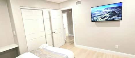 Un dormitorio con cama, televisor, armario y pasillo.