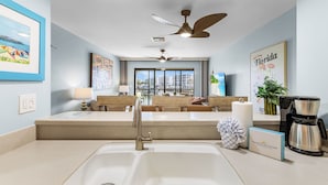 A modern kitchen with a large sink, a coffee maker, and a view of the city through large windows. - Charming Walkable 1BR condo with Canal View and Heated Pool (Fort Myers Beach)