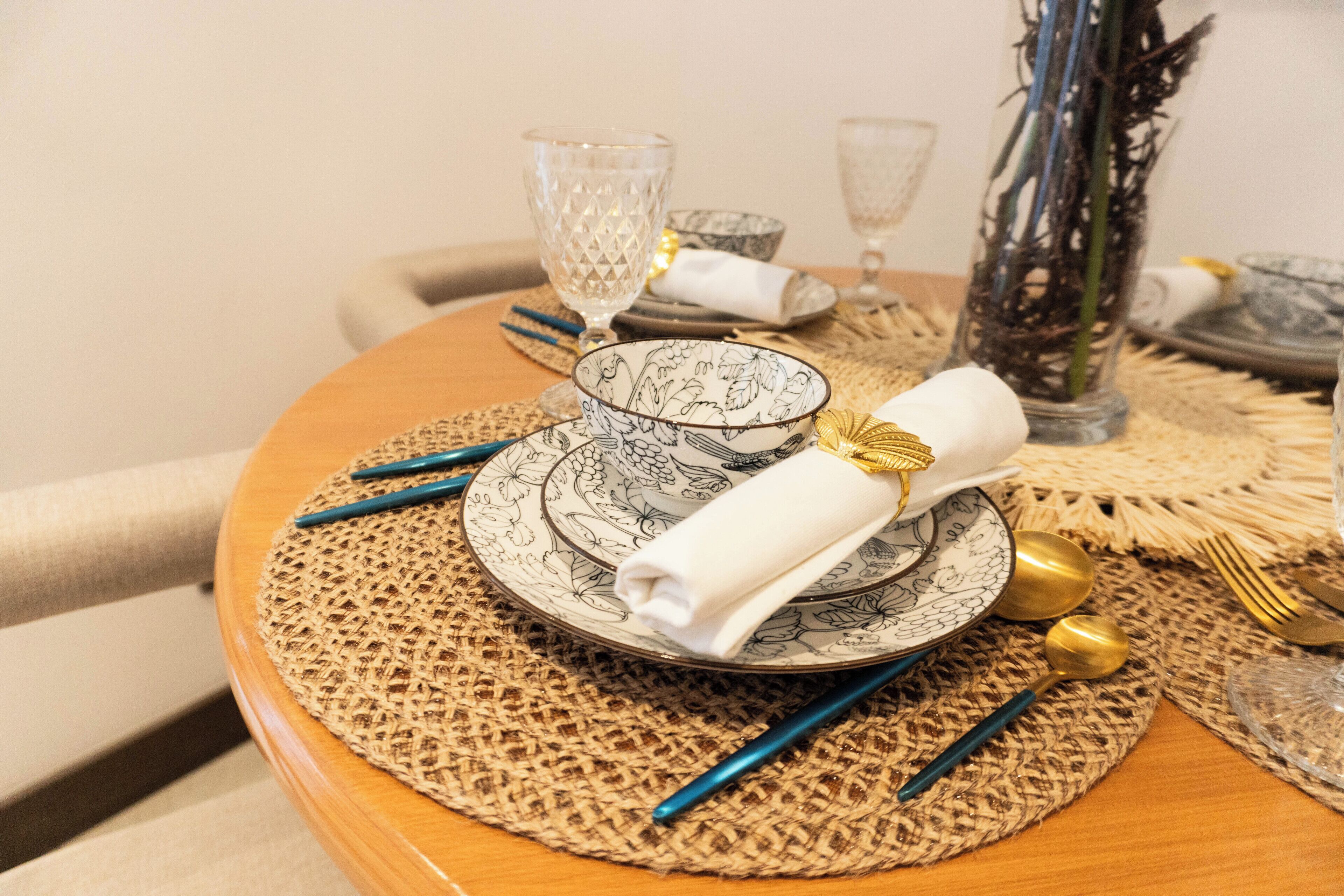 A dining table set with patterned plates, a folded napkin, and blue cutlery.