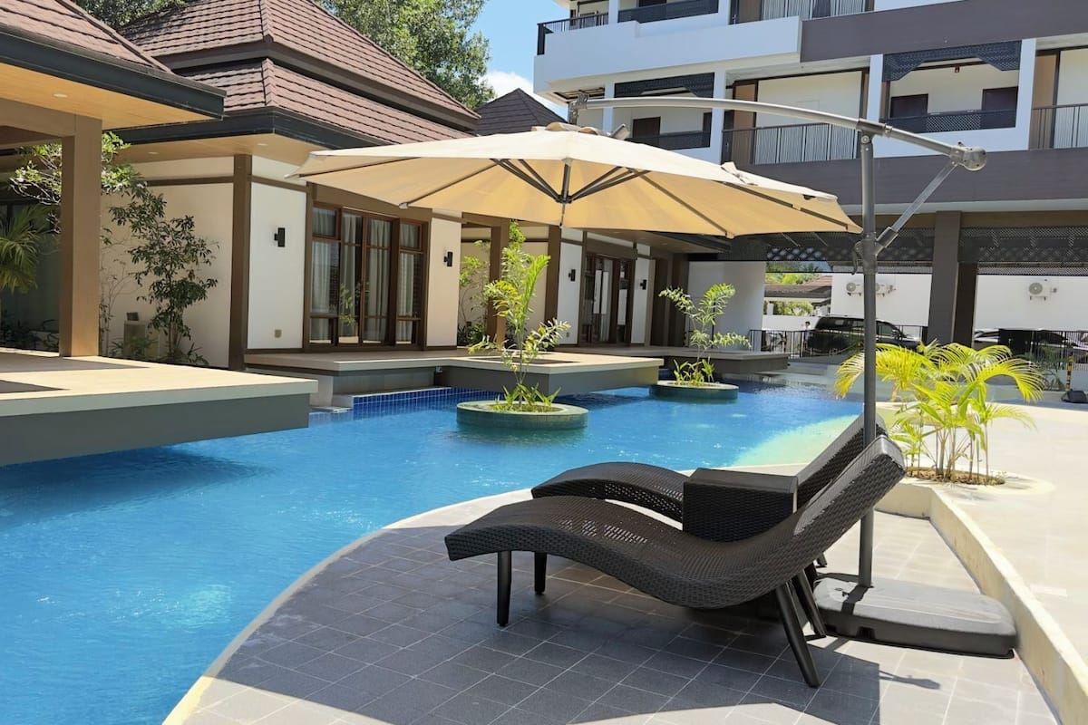 Une piscine avec des chaises longues, un espace de détente couvert et un bâtiment moderne en arrière-plan.