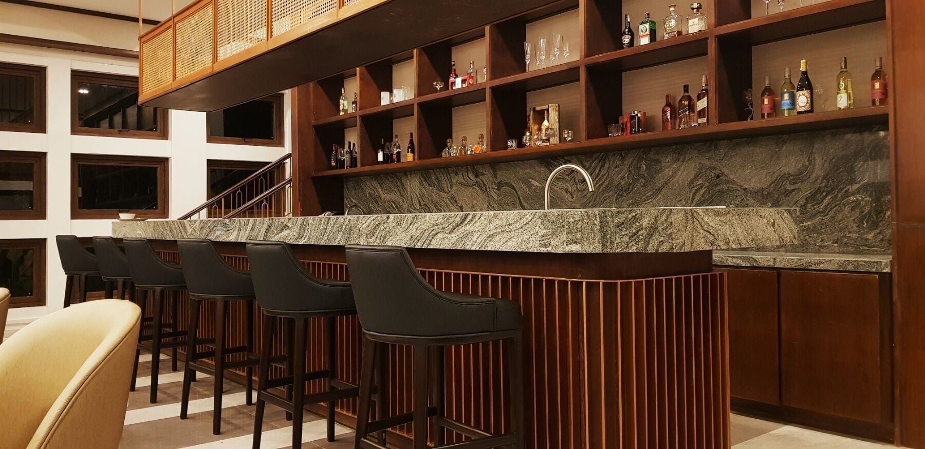 A bar area with a marble countertop, multiple stools, and shelves stocked with bottles and glasses.