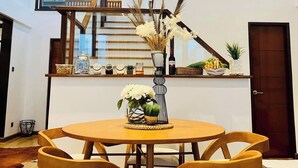 A dining area with a round table, six chairs, a vase with flowers, and a staircase in the background. - Brio De Agoho (Candelaria)