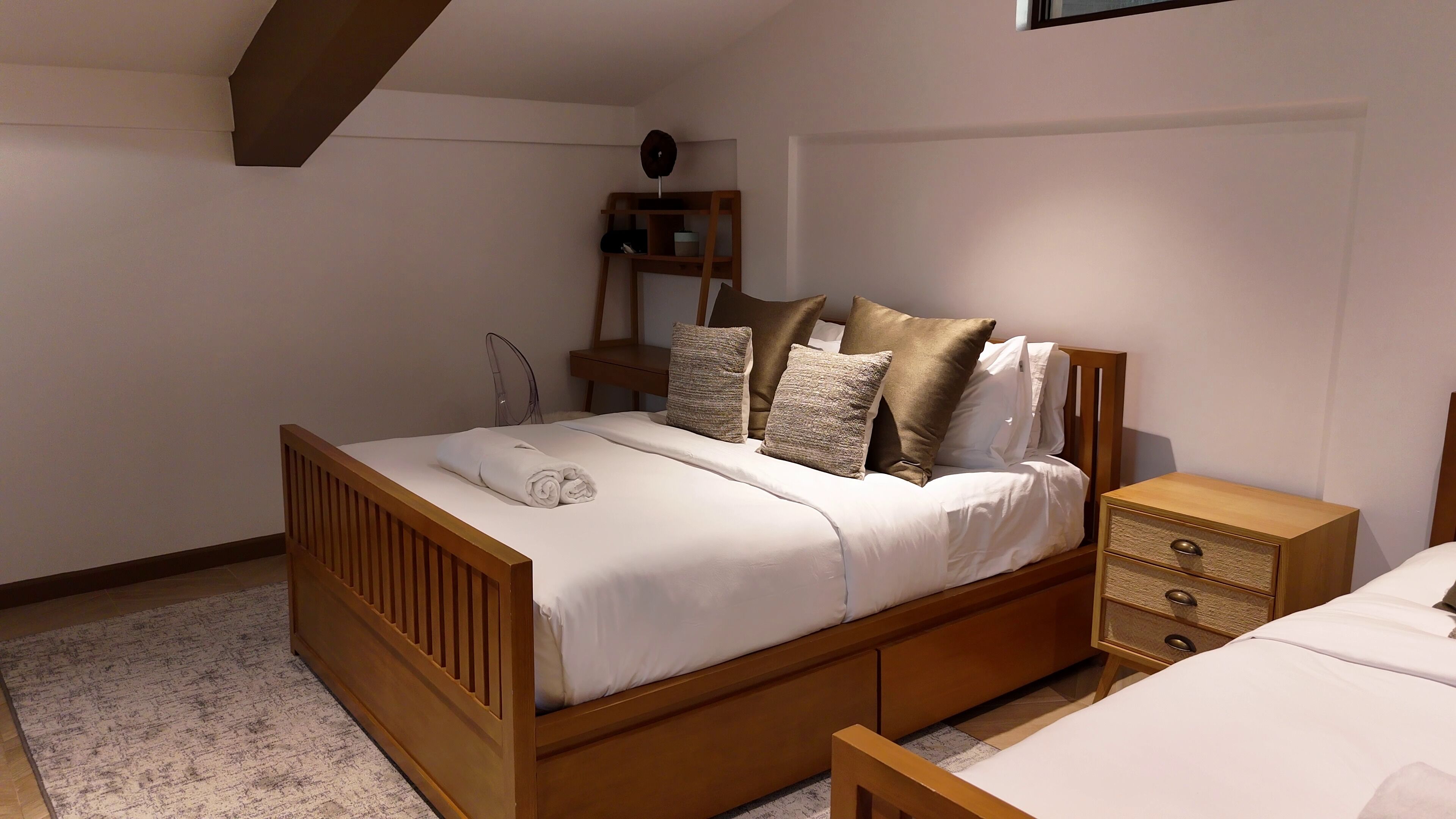 A bedroom with a wooden bed, a nightstand, a bedside table, and a shelf with a clock.