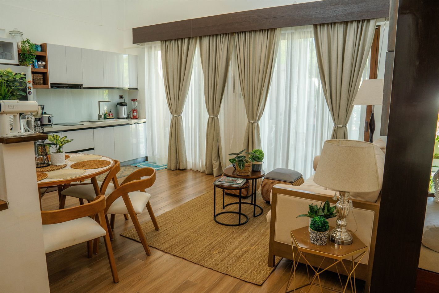 A modern kitchen with white cabinets, a dining area with a round table and chairs, and a cozy seating area with a sofa and a lamp.
