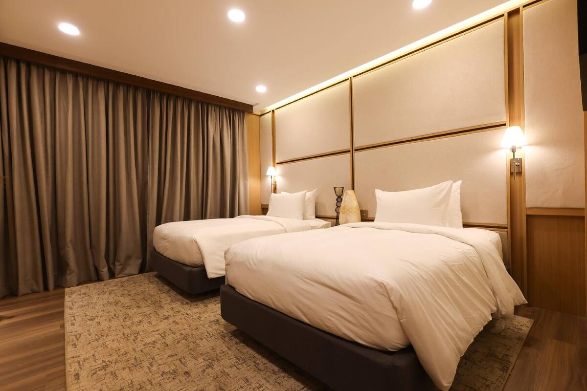 Une chambre d’hôtel avec deux lits, une grande fenêtre avec des rideaux et un plancher en bois.