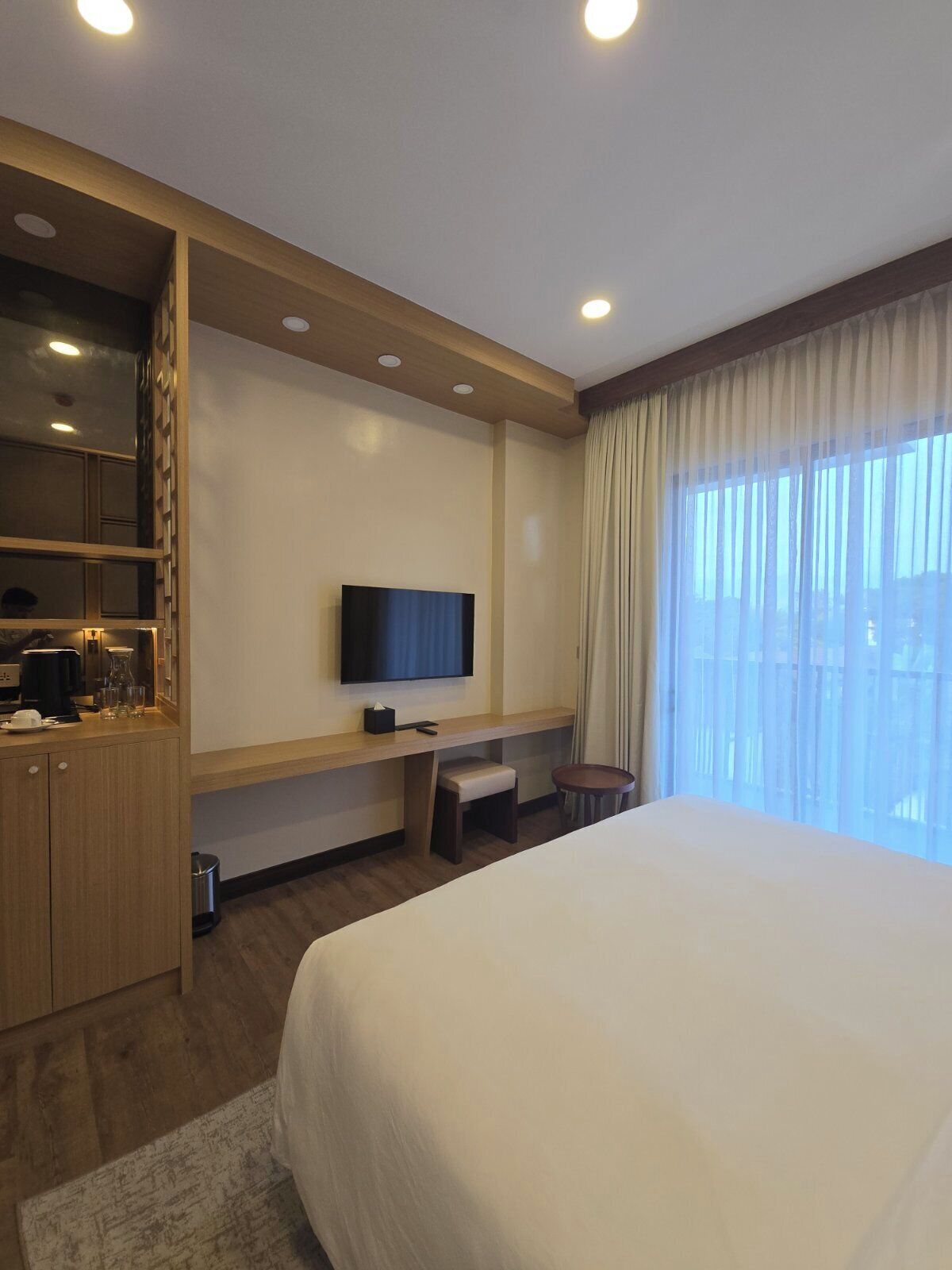 A hotel room with a bed, a TV, a desk, and a window with curtains.