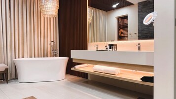 Un baño moderno con una bañera independiente, un espejo grande y un mueble de tocador de madera.
