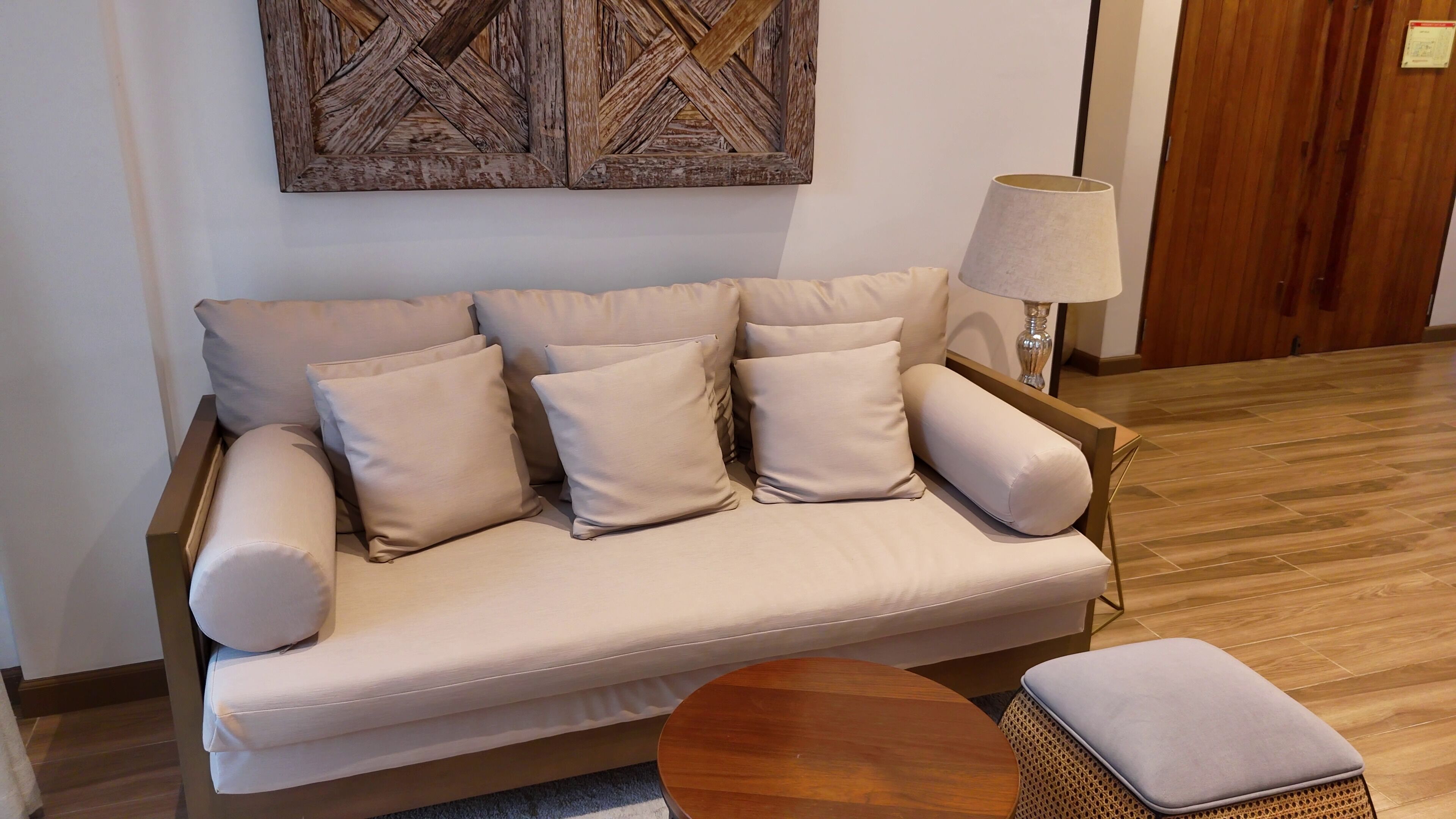 Un sofá beige con varios cojines, una mesa de centro redonda de madera y una lámpara.