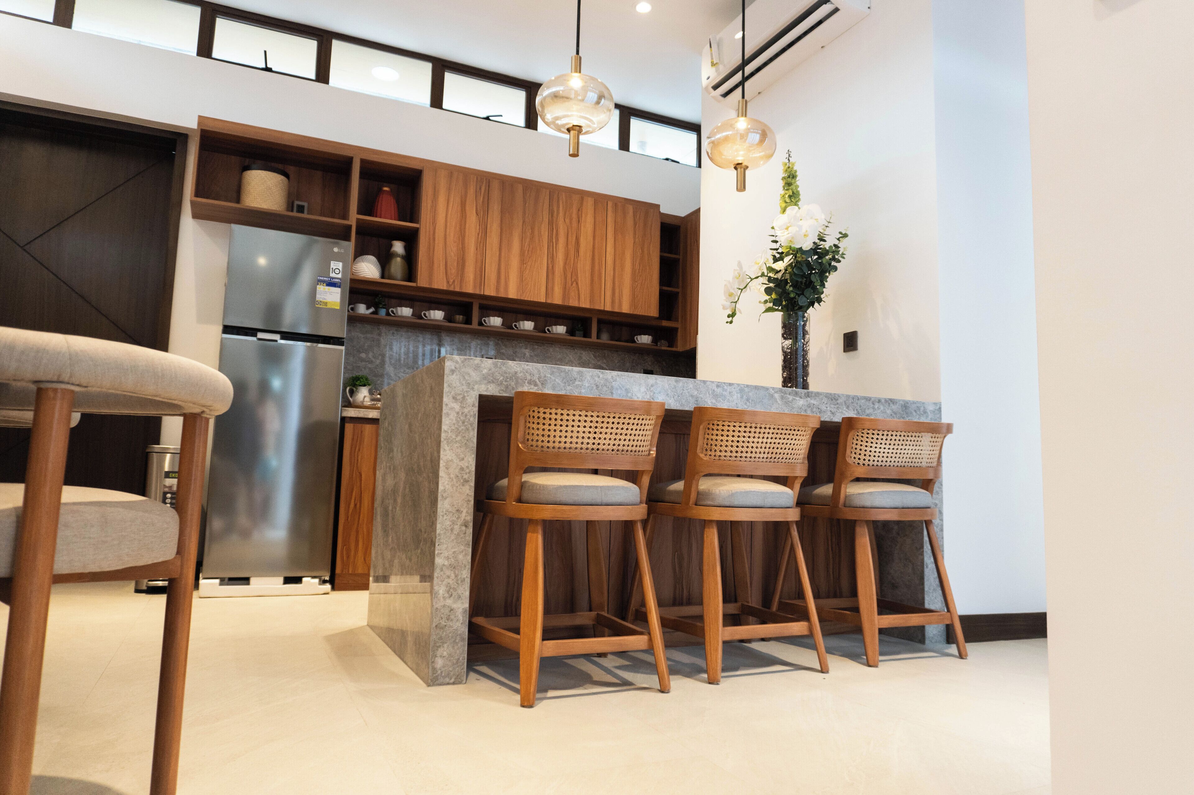 A modern kitchen with wooden cabinets, a built-in refrigerator, and a bar area with stools.