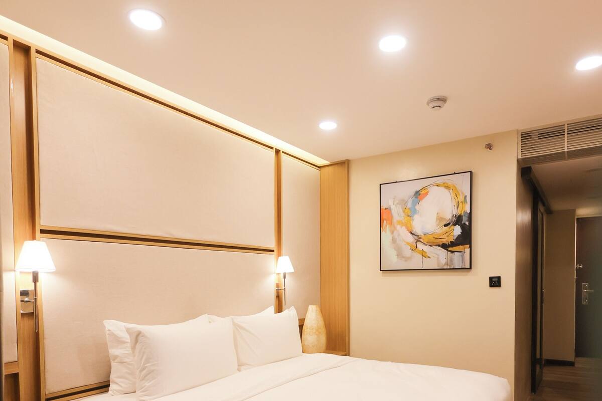 Une chambre d’hôtel moderne avec un grand lit, des spots encastrés au plafond, un tableau au mur et un plancher en bois.